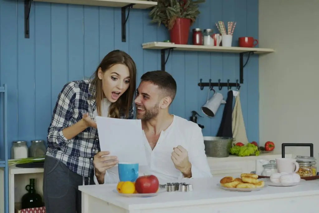 Couple reacting with excitement while reviewing a document at their kitchen table